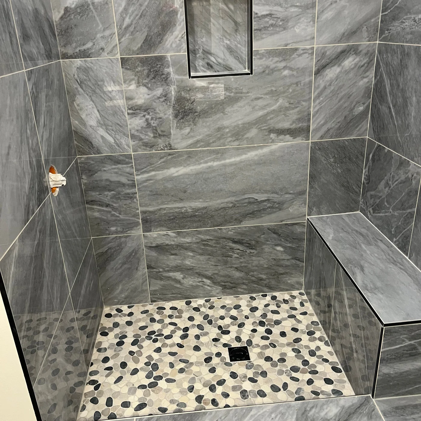 Close view of grey shower tile meeting a small mosaic shower floor