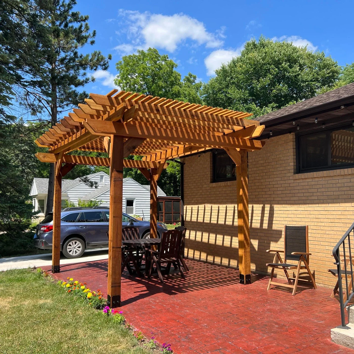 Wood pergola built over a paved patio beside a home
